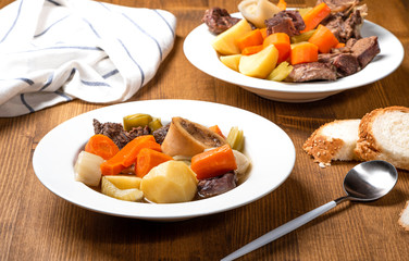 Pot-au-feu popular hot dishes of traditional french cuisine. Braised beef and vegetables with beef broth in a white plate on a wooden table. Winter hot meal.
