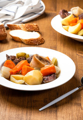 Pot-au-feu popular hot dishes of traditional french cuisine. Braised beef and vegetables with beef broth in a white plate on a wooden table. Winter hot meal.