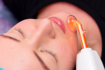 Receiving electric darsonval facial massage procedure at beauty salon