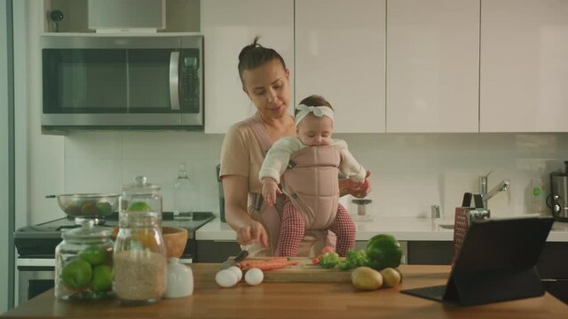 Young mother cook dinner with her little daughter, maternity leave, happy motherhood, showing vegetables to baby
