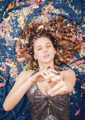 attractive teenager in silver dress lying down on the floor with shiny candy with hands rised up to the camera