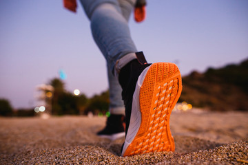 Girl feet in sneakers with bright orange soles go away on the sand. Concept for start, going, step...