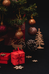Small red gift boxes under the tree, black background, christmas decoration, christmas gifts