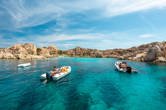 Unidentifiable tourists on small boats in an emerald water gulf - La Maddalena National Park - Parco Nazionale Arcipelago di La Maddalena