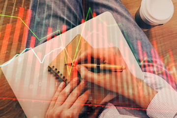 Double exposure of hands writing in notepad with stock market chart.