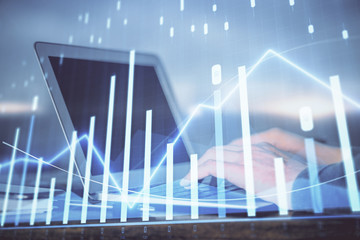 Double exposure of businessman's hands with laptop and stock market graph background. Concept of research and trading.