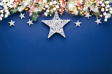 Christmas composition with silver stars and fir branches on blue background.