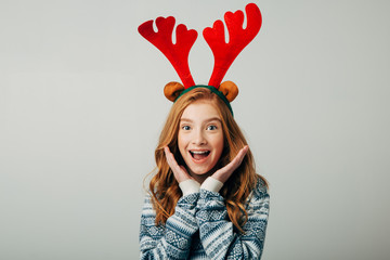 A student girl is very surprised to see such discounts on Christmas presents. A schoolgirl with freckles in a blue sweater is shocked with happiness by surprise. Isolate on a white background.