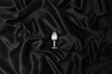 Steel anal plug on a black silk background. Accessories for adult sexual games
