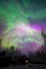 Aurora Borealis corona above old cottage and forest trees