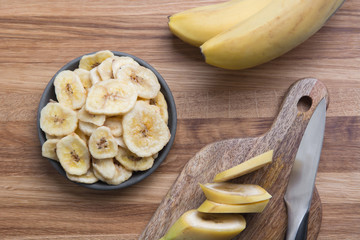 Dehydrated, dried banana chips on wooden board. View from above.