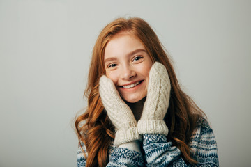 The girl in a sweater smiles, warming her face with gloves on her hands. Warm knitted gloves were very warm and comfortable