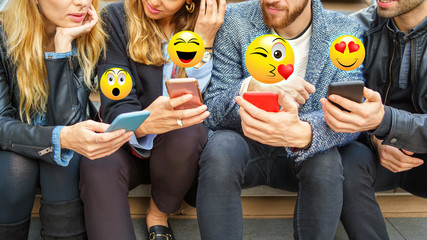 Close up on people hands using smartphones with overlay of emoji faces. Young people using internet and social networks  application concept.