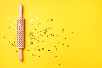 Rolling pin, gold glitter stars on yellow background. Top view. Copy space. Christmas baking concept. Holidays composition. Banner for menu, recipe, ingredients