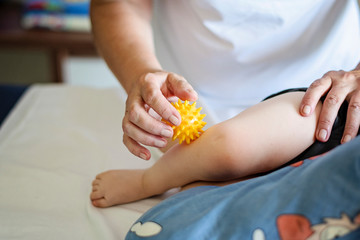 Baby having foot massage in a rehabilitation center. Little child on therapy. Massage therapist massaging a baby with yellow massage ball.