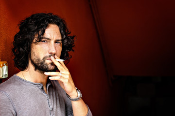 handsome italian young man with long, wavy hair smokes cigarette