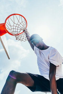 Powerful energetic African American sportsman hanging on basketball lap after scoring ball in net on playground