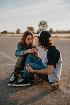 Trendy teenage couple sitting on skates on empty remote road and talking looking at each other
