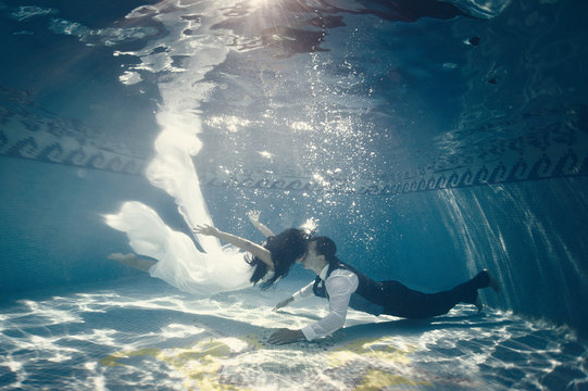 Side view of couple swimming together underwater in swimming pool after wedding ceremony
