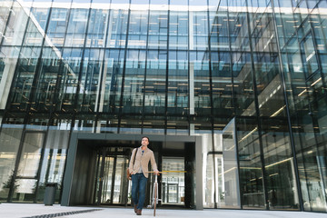Delighted male entrepreneur smiling and walking on the street carrying a bicycle on sunny day in downtown of modern city