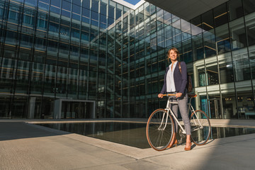Side view of delighted female entrepreneur smiling and riding bike on sunny day in downtown of modern city