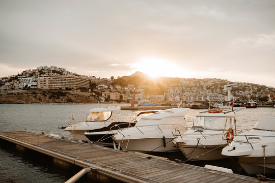 Sea port with white yachts and boats in city with buildings on hills at beautiful sunset with cloudy sky