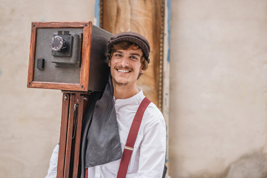 Alcoy, Spain - September, 21 1969: Delighted handsome young man in vintage clothes carrying old fashioned camera and smiling for camera during Modernism Week carnival