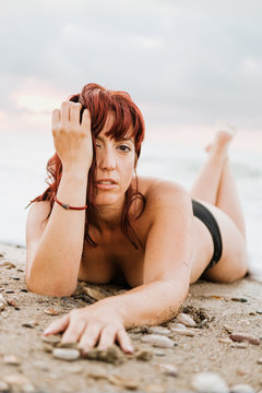 Young nude free calm female posing looking at camera while lying down in a rocky beach
