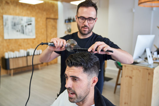 Stock photo of a barber drying hair with a comb and a hairdryer in a barber shop. Barbershop and lifestyle