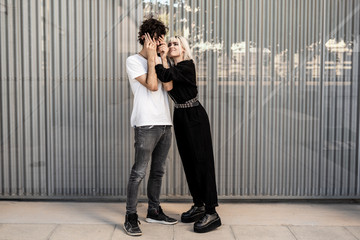 Side view of trendy couple playing with each other against striped wall of modern building