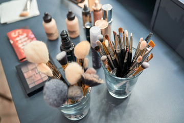 From above different makeup brushes in glasses and eyes shadow with foundation on table in salon
