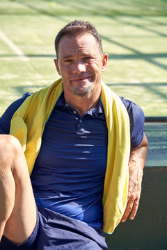 Positive adult sportsman with towel smiling and looking at camera while leaning on border during break on court