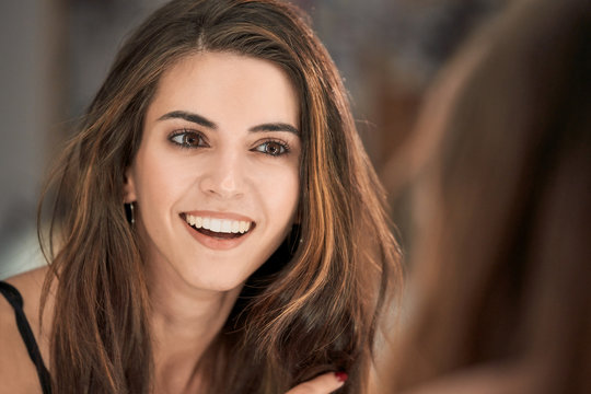 Reflection of charming long haired woman in mirror after cosmetic procedure in salon