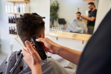 Stock photo of a hands of a barber cutting hair from behind a client's ears with a razor. Barbershop and lifestyle