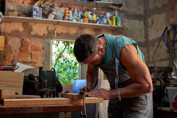 Side view of skilled middle aged handyman in overalls using clamp while working with wooden plank in workshop