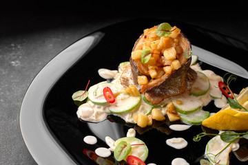 Grilled trout fillet with vegetables, on black background