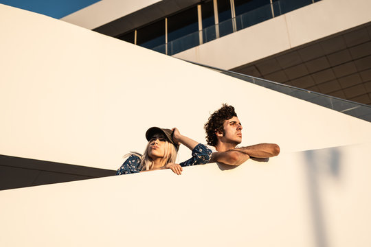 From below displeased stubborn blond woman in hat and proud dark haired man with crossed arms looking away and contemplating after disagreement on stairs