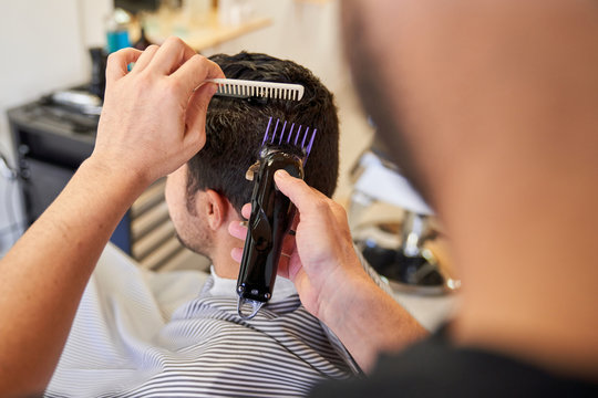 Stock photo of a barber cutting hair with a machine to a customer sitting on the barber chair