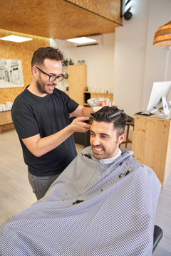 Stock vertical photo of a barber cutting a client's hair with a razor. Barbershop and lifestyle