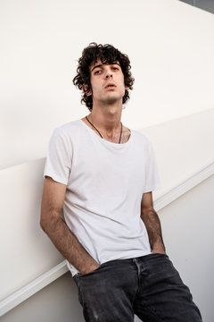 From below handsome confident dark haired man in casual clothes looking at camera against white wall