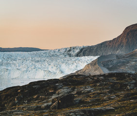 People sitting standing in front of huge glacier wall of ice. Eqip Sermia Glacier Eqi glacier in Greenland called the calving glacier during midnight sun. Hikers during travel and vacation.