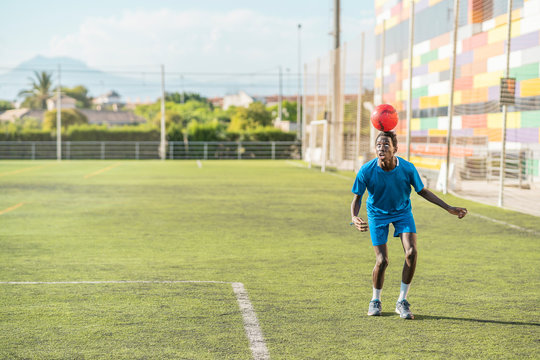 Skinny black teenager jugging football ball on head