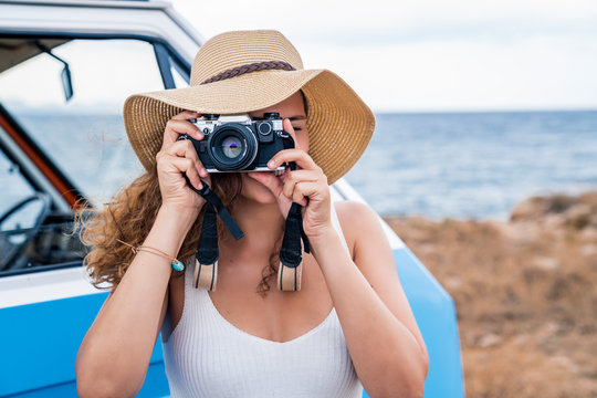 Active enthusiastic lady in hat photographing on camera in hands nearby blue car on beach
