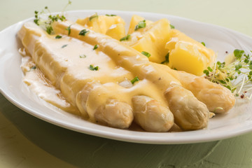 white asparagus poured with .hollandaise sauce, potatoes with chives and sprouts.