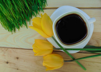 cup of coffee and yellow tulips on wooden table
