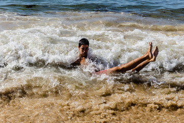 A young guy swims in the spray of the sea. He is laughs and scream..