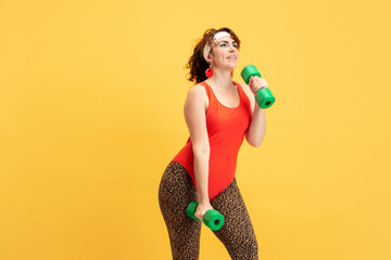 Young caucasian plus size female model's training on yellow background. Copyspace. Concept of sport, healthy lifestyle, body positive, fashion, style. Stylish woman practicing with the weights.
