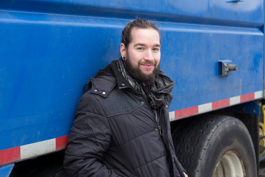 Medium Horizontal View Of Young Smiling Bearded Man In Checkered Shirt And Hair Tied Back Leaning Against Large Blue Truck, Quebec City, Quebec, Canada