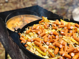 Hunting sausages with potatoes and onions in pan on fire 