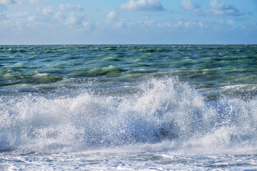 White spray of a wave breaking on the beach with a rough sea and sky behind